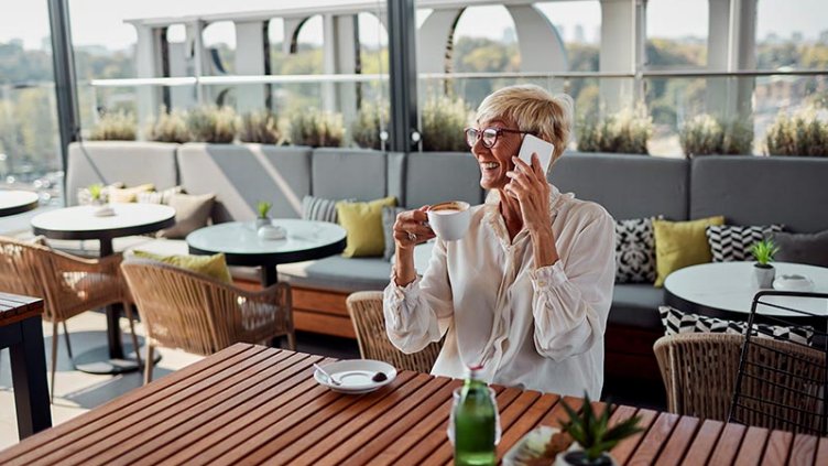 A woman sitting on a chair in a hotel and having a cup of tea, smiling while talking on phone